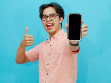 Asyalı adam mavi arkaplanda boş ekranlı cep telefonu gösteriyor