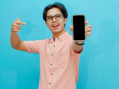 Asyalı adam mavi arkaplanda boş ekranlı cep telefonu gösteriyor