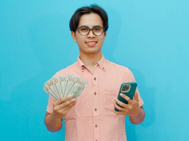 Elinde para ve cep telefonu tutarken mutlu gülümseyen bir adam