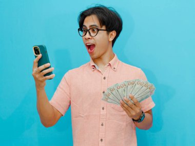 Heyecanlı Asyalı işadamı elinde para ve cep telefonu tutarken şaşırmış..