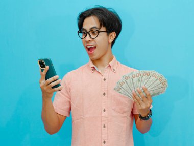 Heyecanlı Asyalı işadamı elinde para ve cep telefonu tutarken şaşırmış..