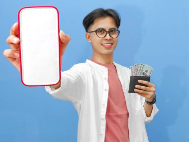 Sıradan kıyafetler içinde Asyalı bir adam cüzdan dolusu para tutuyor ve mavi arka planda dostane bir gülümsemeyle boş bir telefon ekranı gösteriyor..