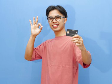 Asyalı bir adam kredi kartı tutuyor, mutlu bir ifadeyle 