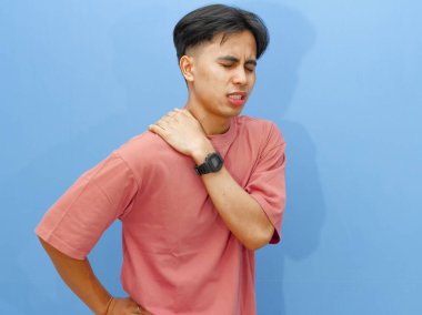 Sağlıksız bir gencin portresi belini ve sırtını tutarken hüzünlü ve acı verici bir ifadeyle izole edilmiş mavi bir arka planda..