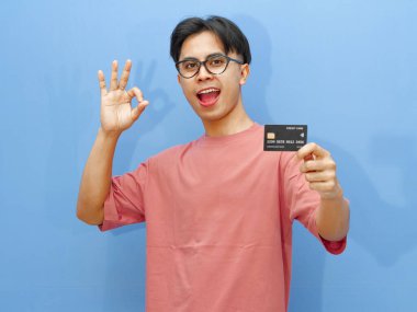 Asyalı bir adam kredi kartı tutuyor, mutlu bir ifadeyle 
