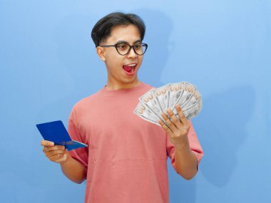 Elinde para olan mutlu Asyalı bir adamın portresi ve mavi arka planda soyutlanmış, şok olmuş bir ifadeyle banka tasarruf defterine bakması..