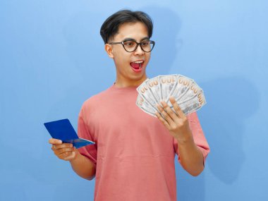 Elinde para olan mutlu Asyalı bir adamın portresi ve mavi arka planda soyutlanmış, şok olmuş bir ifadeyle banka tasarruf defterine bakması..