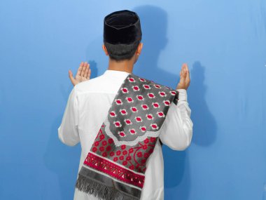 Müslüman kıyafetli Asyalı Müslüman adamın mavi arka planda Tanrı 'ya dua edişinin arkası.