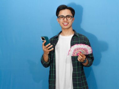 Bir cep telefonu tutarak poz veren ve mutlu bir yüz ifadesi gösteren Asyalı genç bir adamın portresi..