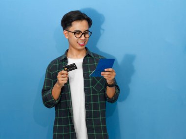 Genç Asyalı adam elinde kredi kartı tutarken mutlu bir şekilde tasarruf defterini kontrol ediyor ve olumlu bir mali tavır sergiliyor..