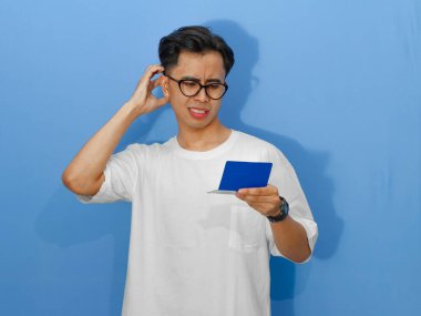 Beyaz tişörtlü endişeli bir Asyalı banka tasarruf defterine bakarken düşünceli bir hareket gösteriyor..