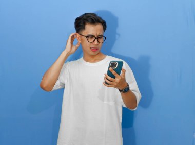 Beyaz tişörtlü Asyalı genç bir adamın portresi. Elinde cep telefonu tutarken mutsuz ve düşünceli görünüyor.