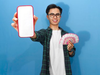 Mutlu Asyalı adam elinde cep telefonu ve para gösteren boş bir ekran tutuyor.