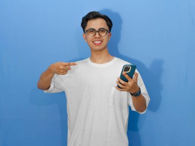 Elinde cep telefonu tutan beyaz tişörtlü gülümseyen Asyalı genç bir adamın portresi. Reklam, iletişim ve teknoloji kavramları için mükemmel..