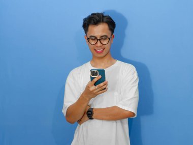 Elinde cep telefonu tutan beyaz tişörtlü gülümseyen Asyalı genç bir adamın portresi. Reklam, iletişim ve teknoloji kavramları için mükemmel..