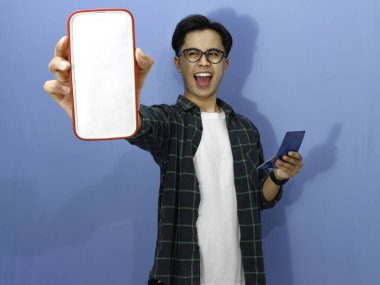 Boş bir cep telefonu ekranı gösterirken elinde banka tasarruf kitabı tutan sıradan tişörtlü genç Asyalı hayret verici bir adam..