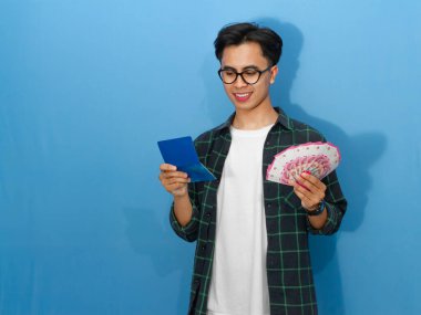 Elinde para tutarken gülümseyen genç bir Asyalı adamın portresi. Tasarruf defterine bakıyor. Mali durumundaki heyecan ve güveni gösteriyor..