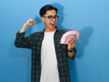 Sıradan gömlekli genç bir Asyalı 'nın portresi para tutuyor, yumruklarını sıkıyor ve başarıyı heyecanlı bir ifadeyle kutluyor..