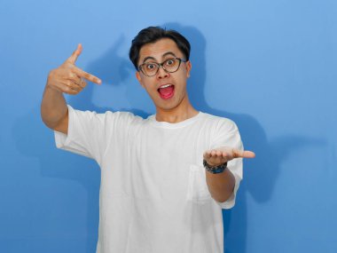 Beyaz tişörtlü heyecanlı Asyalı genç adam, pazarlama ve reklamcılık için mükemmel olan avucunu gösterirken hayret verici bir ifade sergiliyor..