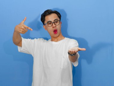 Beyaz tişörtlü heyecanlı Asyalı genç adam, pazarlama ve reklamcılık için mükemmel olan avucunu gösterirken hayret verici bir ifade sergiliyor..