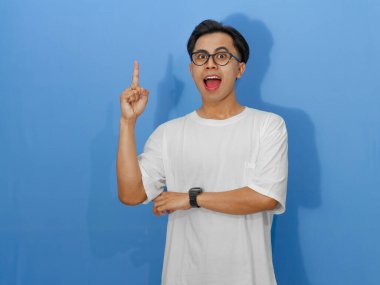 Beyaz tişörtlü genç bir Asyalı 'nın portresi, heyecanlı bir ifade sergiliyor ve parlak bir fikir ediniyormuş gibi işaret ediyor..