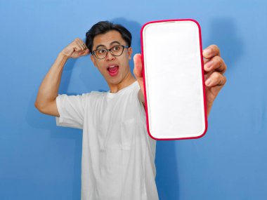 Beyaz tişört giyen genç bir Asyalı 'nın portresi. Başarı kutlamalarında yumruklarını sıkarken boş bir cep telefonu ekranını heyecanla gösteriyor..