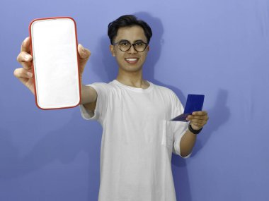 Beyaz gömlekli genç Asyalı adam elinde banka tasarruf defteri tutarken boş bir cep telefonu ekranı gösteriyor. Reklam, finans veya bankacılık kavramları için mükemmel..