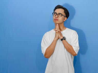 Beyaz tişörtlü genç Asyalı bir adam düşünceye dalmış, hangi kararı vereceği konusunda kuşkulu ve şaşkın görünüyor..