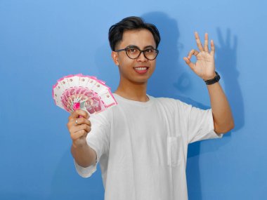 Beyaz tişörtlü, Asyalı genç bir adam mutluluğu ve güveni yansıtan iyi bir parmak izi gösteriyor..