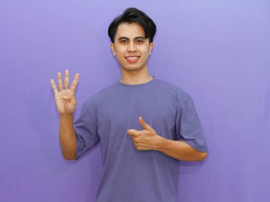 Gülümseyen mutlu Asyalı bir adamın portresi. İzole edilmiş mor bir arka plana başparmak atarken dört parmağını gösteriyor..