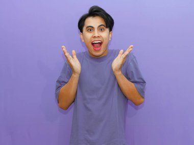 Şok olmuş bir ifadeyle genç bir Asyalı, mor arka plandaki kameraya bakıyor. Reklam, ifade kavramları ve promosyonlar için ideal..