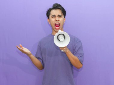 Kızgın genç Asyalı bir adam megafonla bağırıyor, mor bir arka planda hayal kırıklığını ifade ediyor. Reklam, protesto ya da motivasyon kavramları için mükemmel..
