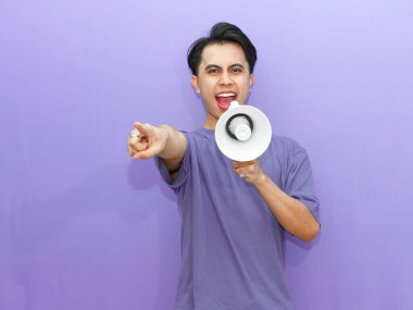 Elinde megafon tutan enerjik genç Asyalı bir adam heyecanlı bir ifadeyle kameraya bağırıyor ve işaret ediyor. Mor arka planda promosyonlar ve reklamlar için mükemmel..