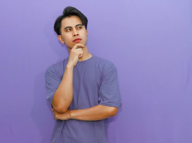 Ciddi bir Asyalı adam, düşünceli bir jest yapıyor, izole edilmiş mor bir arka plana bakıyor..