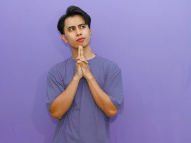 Ciddi bir Asyalı adam, düşünceli bir jest yapıyor, izole edilmiş mor bir arka plana bakıyor..