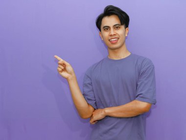 Mutlu bir Asyalı genç adamın portresi canlı mor bir arka plana karşı yan tarafı gösteriyor..