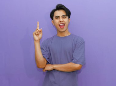 Heyecanlı genç Asyalı bir adam, parlak mor bir arka plana karşı bir fikir jesti sergiliyor..