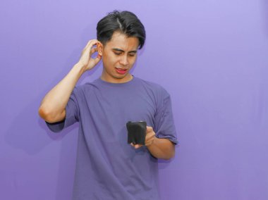 Zavallı Asyalı genç adam boş bir cüzdan tutuyor, mor arka planda ağlayan bir jest gösteriyor, finansal zorlukları vurguluyor..