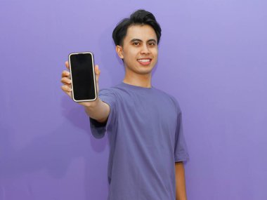 Mutlu genç Asyalı adam canlı mor bir arka planda boş cep telefonu ekranı gösteriyor. Reklam ve tanıtım amaçlı kullanım için mükemmel..