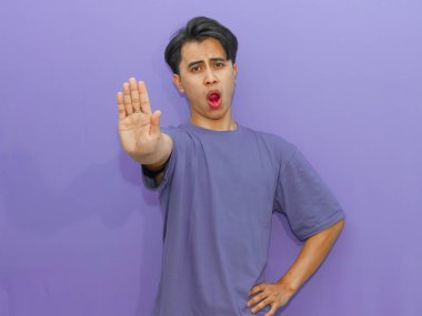 Kızgın genç Asyalı bir adam, eli parlak mor bir arka planda, dur hareketi yapıyor. Reklam için mükemmel..