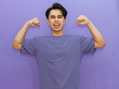 Gururlu genç Asyalı adam güçlü bir jestle kaslarını esnetiyor, canlı mor bir arka plana gülümsüyor..