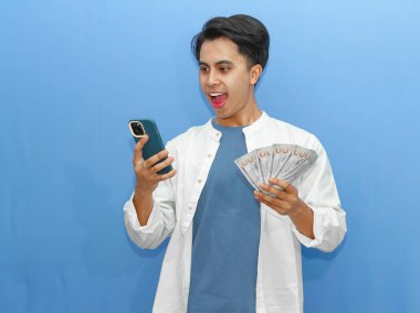 Genç bir Asyalı adam cep telefonu kullanırken ve elinde banknotlar tutarken şaşırmış görünüyor..