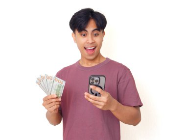 Mutlu Asyalı genç adam elinde akıllı telefon ve nakit tutarak şaşırdı. Heyecanlı ifade tarzı, sade bir arka planda izole, finans, iş ve reklam teması için mükemmel..