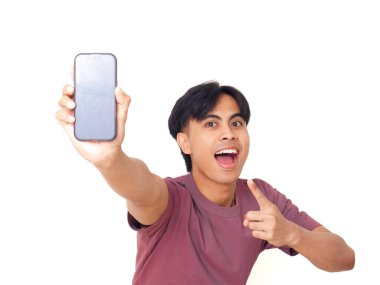 Mutlu Asyalı genç adam gülümsüyor ve boş akıllı telefon ekranına işaret ediyor. İzole edilmiş beyaz arka planda reklam için kopya alanı sunuyor..