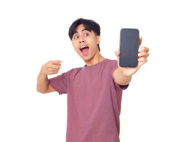 Mutlu Asyalı genç adam gülümsüyor ve boş akıllı telefon ekranına işaret ediyor. İzole edilmiş beyaz arka planda reklam için kopya alanı sunuyor..