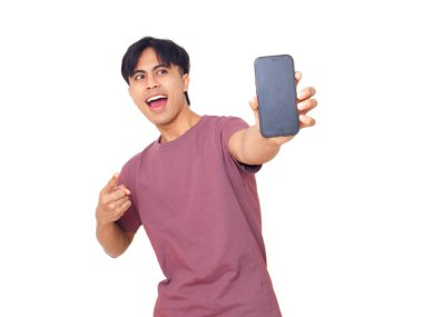 Mutlu Asyalı genç adam gülümsüyor ve boş akıllı telefon ekranına işaret ediyor. İzole edilmiş beyaz arka planda reklam için kopya alanı sunuyor..