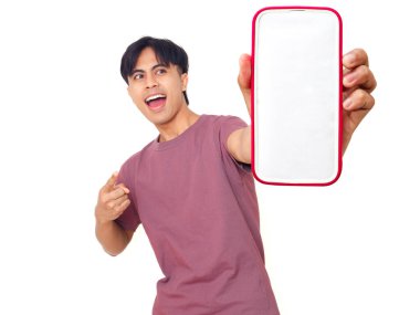 Mutlu Asyalı genç adam gülümsüyor ve boş akıllı telefon ekranına işaret ediyor. İzole edilmiş beyaz arka planda reklam için kopya alanı sunuyor..