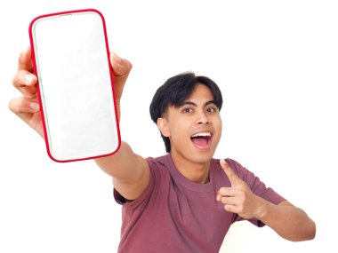 Mutlu Asyalı genç adam gülümsüyor ve boş akıllı telefon ekranına işaret ediyor. İzole edilmiş beyaz arka planda reklam için kopya alanı sunuyor..