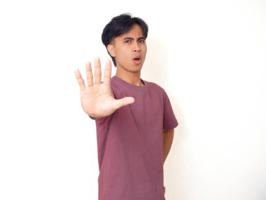 Ciddi Asyalı genç adam sert bir ifadeyle el hareketi yapıyor, sade bir arka planda izole edilmiş, uyarı, reddetme, ihtiyat veya yasaklama kavramı..