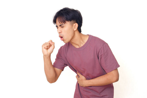 Young Asian man coughing and holding stomach with painful expression on plain background, suitable for health, illness, medical concept, and healthcare advertising.
